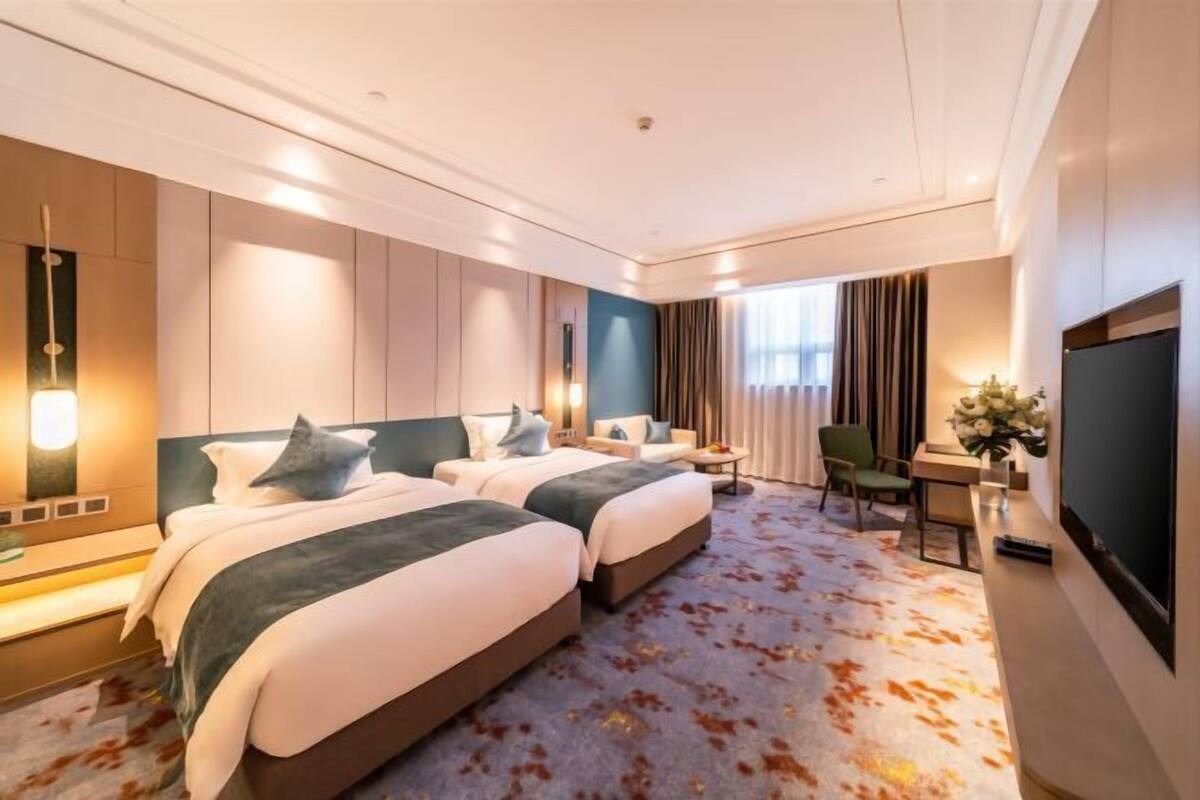 Une chambre d’hôtel avec deux lits, un bureau, une chaise, une télévision et une grande fenêtre.