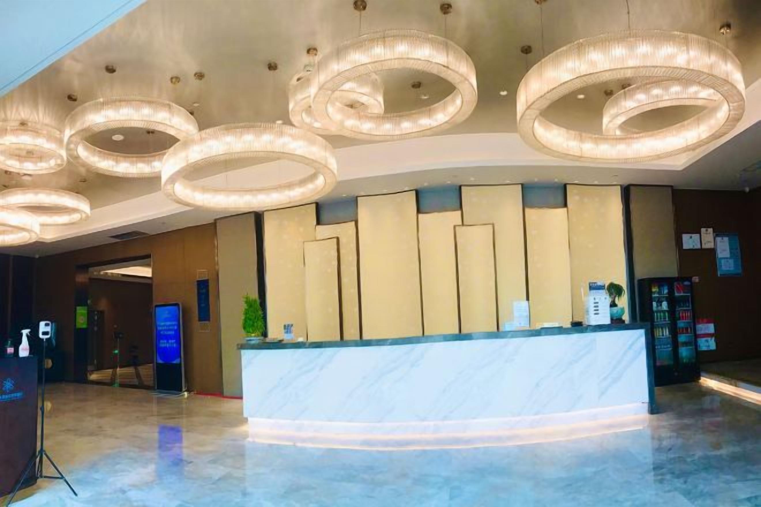 Zona de recepción de hotel con mostrador de mármol, luminarias modernas y un panel informativo digital.