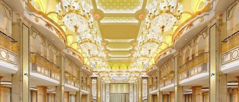 A grand hall with rows of tables and chairs, ornate ceiling, and chandeliers.