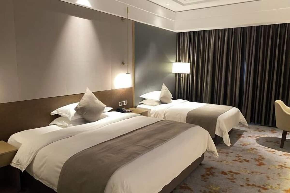 Une chambre d’hôtel avec deux lits, une table de chevet, une lampe et un rideau.