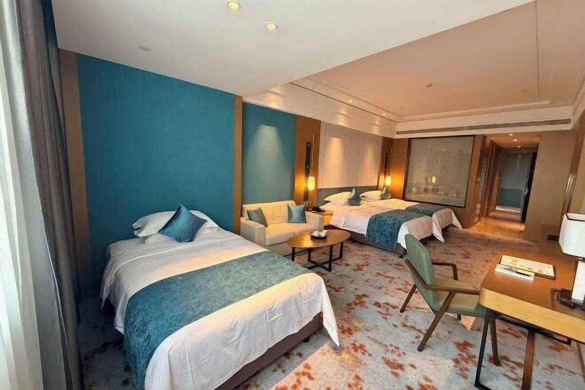 Une chambre d’hôtel avec deux lits, un canapé, une table et une grande fenêtre.
