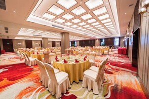 Un salón de banquetes con mesas redondas, sillas blancas y una alfombra roja.