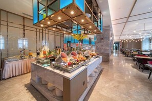 Montaje de bufé con distintos alimentos, una zona de servicio central y un área de estar con mesas y sillas.