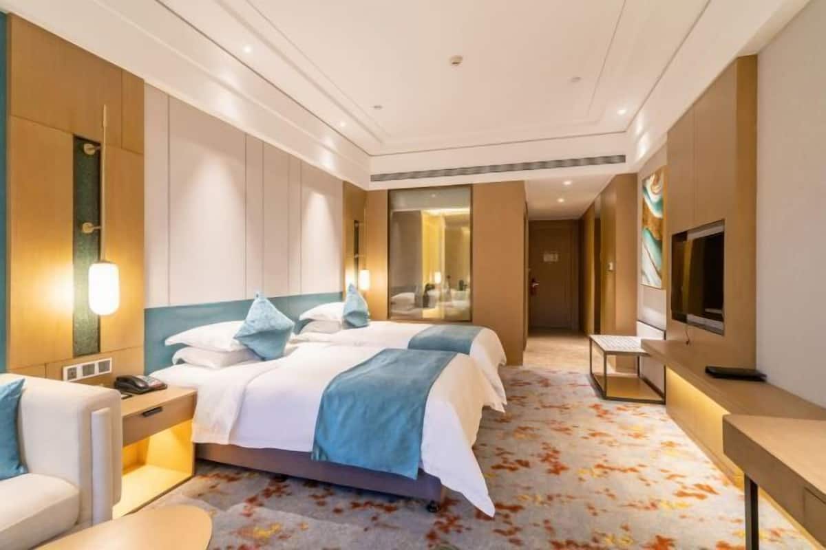 Une chambre d’hôtel avec deux lits, un bureau, une chaise, une télévision et une salle de bain visible à travers une porte en verre.