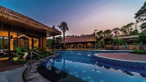 Piscina com estrutura de telhado de palha e um edifício com grandes janelas.