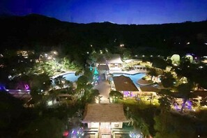 Un complejo turístico con varias piscinas, un edificio central y árboles circundantes.