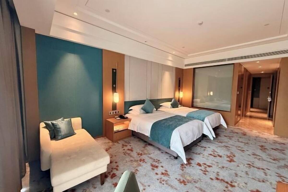 Une chambre d’hôtel avec deux lits, un canapé, une table de chevet et une grande fenêtre.
