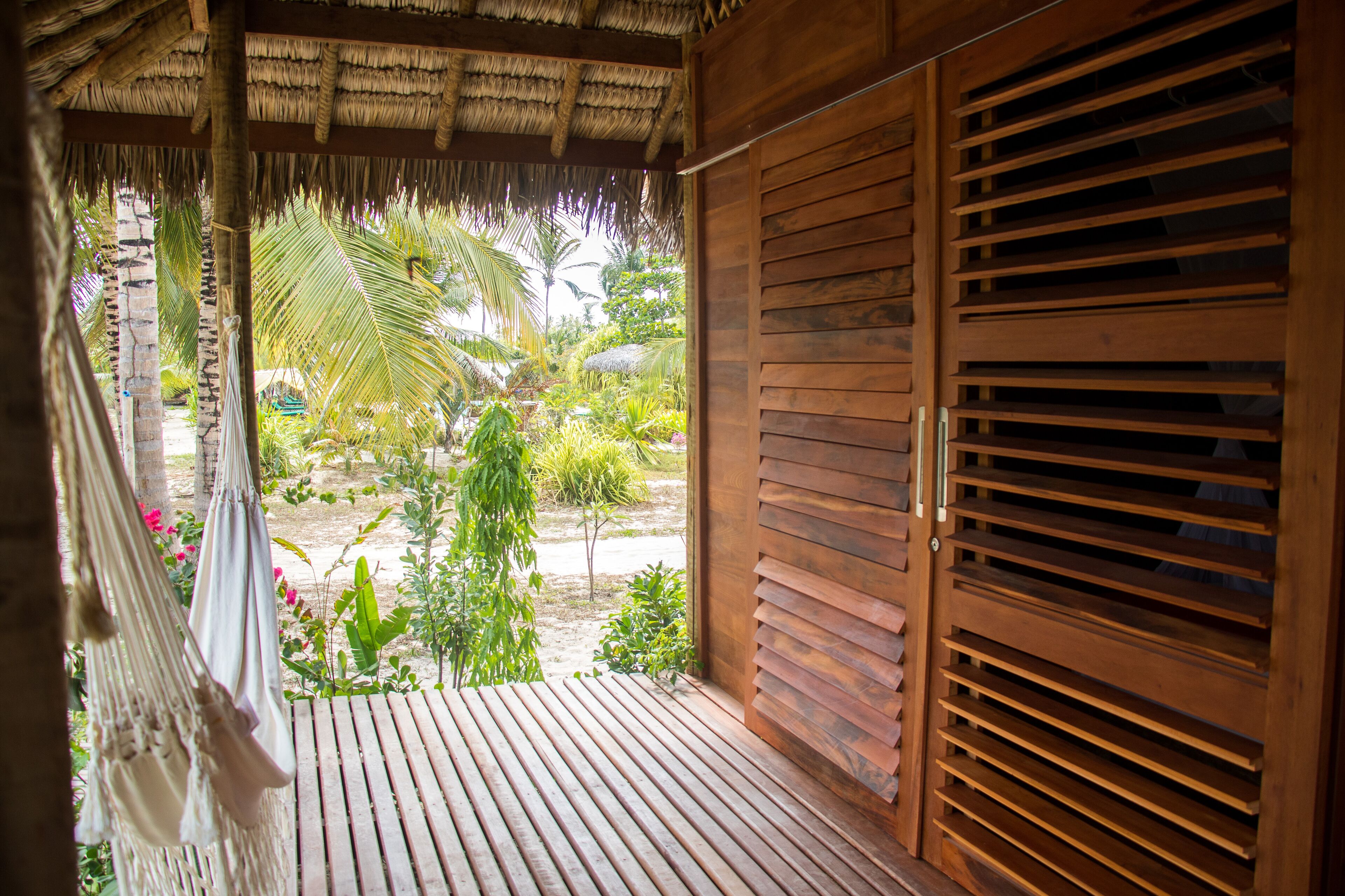 Un balcon en bois doté d’un toit de chaume, d’un hamac et offrant une vue sur la végétation tropicale.