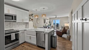 Une cuisine moderne avec des meubles blancs, un îlot central et un four à micro-ondes. Un coin repas offre une vue sur l’océan.