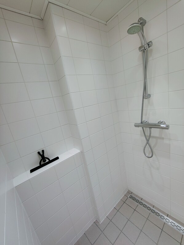 A bathroom with white tiled walls, a shower with a handheld showerhead, and a towel rack.