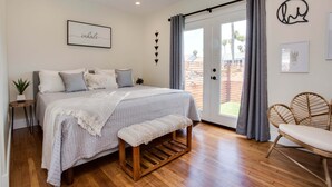A bedroom with a bed, bench, bedside table, and a view of the outside.