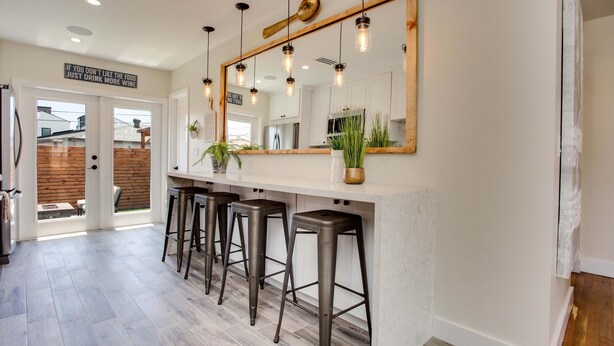 A modern kitchen with a large mirror, bar stools, and a sign above the door.