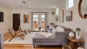 A modern living room with a grey sofa, wooden chairs, a white rug, and a large mirror.