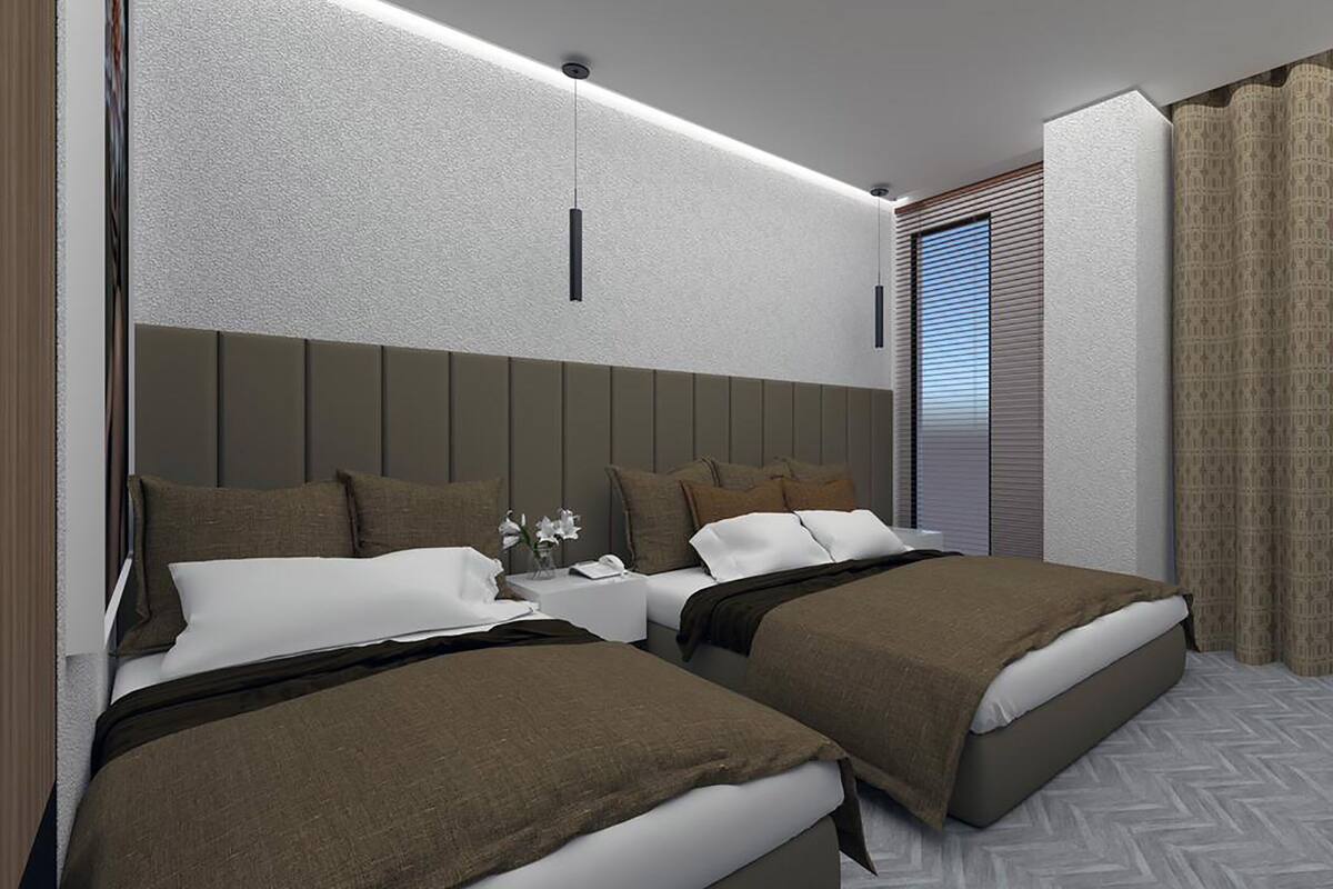 Ein Hotelzimmer mit zwei Betten, einem Nachttisch, einer Hängelampe, einem Fenster mit Jalousien und gemusterten Vorhängen.