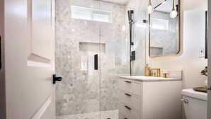A modern bathroom with a glass-enclosed shower, a white vanity with gold fixtures, and a large mirror. - Dream HOUSE❤️ Walk to Beach & Bay - Hot Tub + AC + FirePit + Bikes (San Diego)
