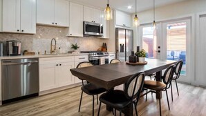 A modern kitchen with white cabinets, stainless steel appliances, and a central island with chairs. - Dream HOUSE❤️ Walk to Beach & Bay - Hot Tub + AC + FirePit + Bikes (San Diego)