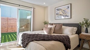 A bedroom with a bed, a nightstand, a framed picture, and a sliding glass door leading to a balcony. - Dream HOUSE❤️ Walk to Beach & Bay - Hot Tub + AC + FirePit + Bikes (San Diego)