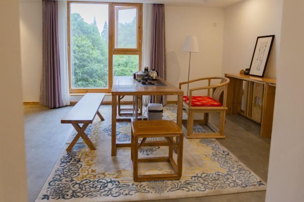 A room with a wooden table, bench, and chair, a patterned rug, a window with curtains, and a lamp.