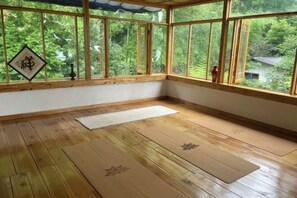 A room with wooden flooring, tatami mats, a large window with a view of greenery, and a decorative item on the wall.