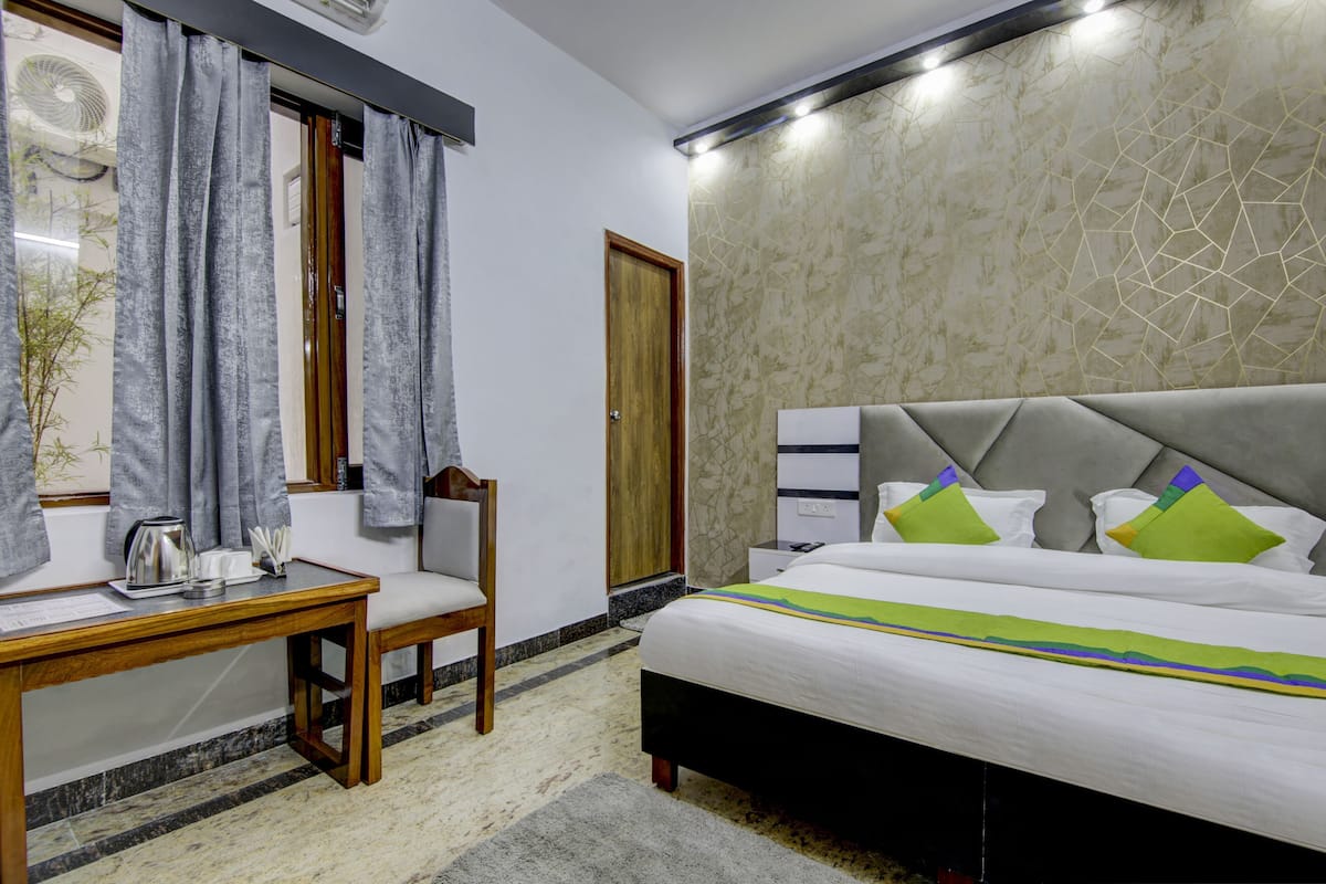 A hotel room with a bed, bedside table, chair, and a window with curtains.