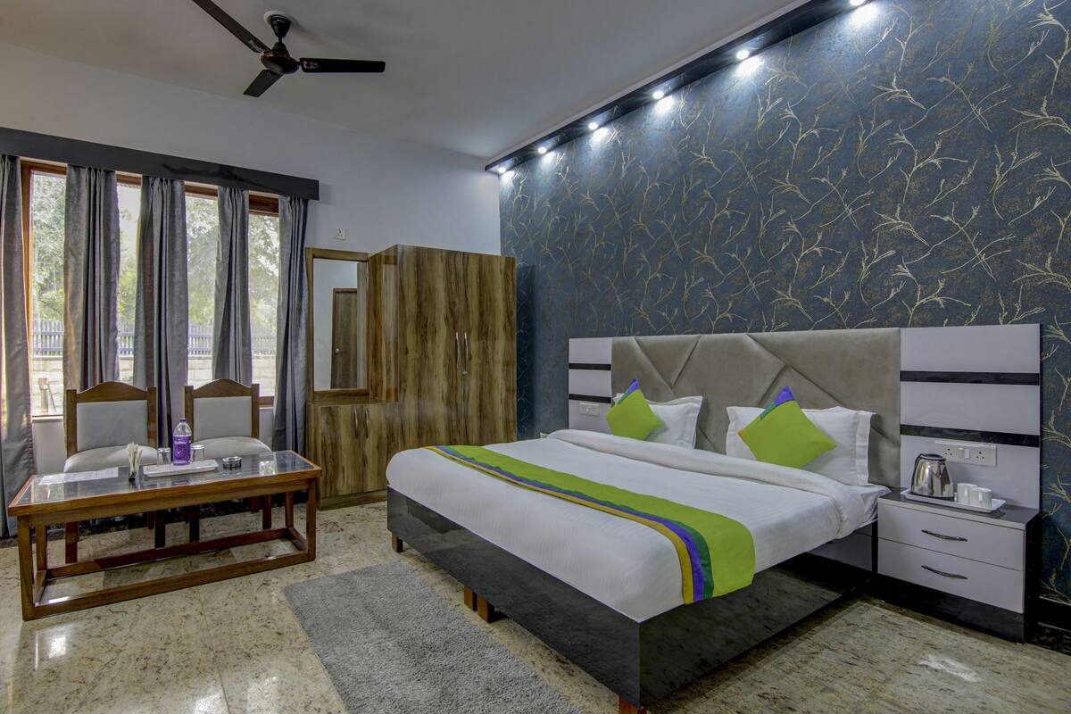 A hotel room with a bed, bedside table, and a desk with chairs.