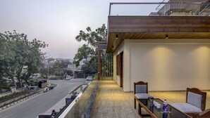 A balcony with a glass railing overlooking a street, a table with chairs, and a bottle of water. - Treebo Sai Village, Manesar (Gurugram)