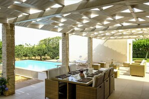 Relax by the pool in this serene outdoor space, featuring a wicker dining set and a geometric ceiling.