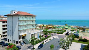 A multi-story building with balconies, a parking area, and a view of the sea. - Little Hotel (Cesenatico)