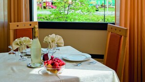 A dining table set with a bottle, a bowl of fruit, and a glass. - Little Hotel (Cesenatico)