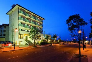 A multi-story hotel with a modern design, featuring balconies on each floor, a well-lit entrance, and a clear view of the street. - Little Hotel (Cesenatico)