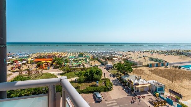 A beachside view with a parking area, beach umbrellas, and a small building. - Little Hotel (Cesenatico)