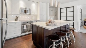 Een moderne keuken met witte kastjes, roestvrijstalen apparatuur en een centraal kookeiland met krukken.