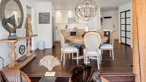 Een moderne eetruimte met een ronde houten tafel, witte beklede stoelen en een centrale kroonluchter.
