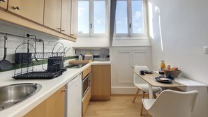 A compact kitchen with wooden cabinets, a sink, a toaster, and a dining area with a table and chairs.