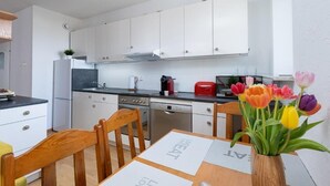 A modern kitchen with white cabinets, a black countertop, and a dining area with a wooden table and chairs. There is a vase with tulips on the table.