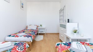 A small, bright room with two beds, a desk, and a dresser.