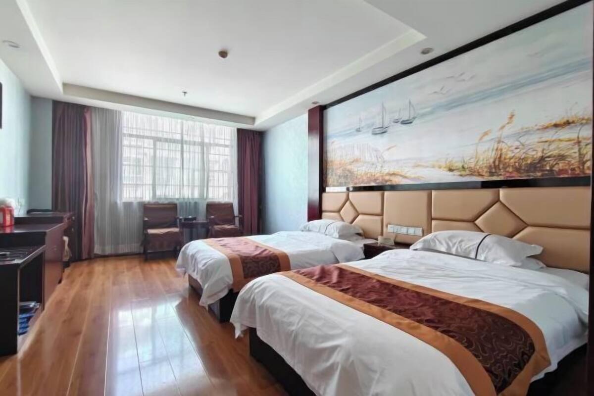 Ein Hotelzimmer mit zwei Betten, einem Schreibtisch, einem Stuhl und einem großen Gemälde an der Wand.