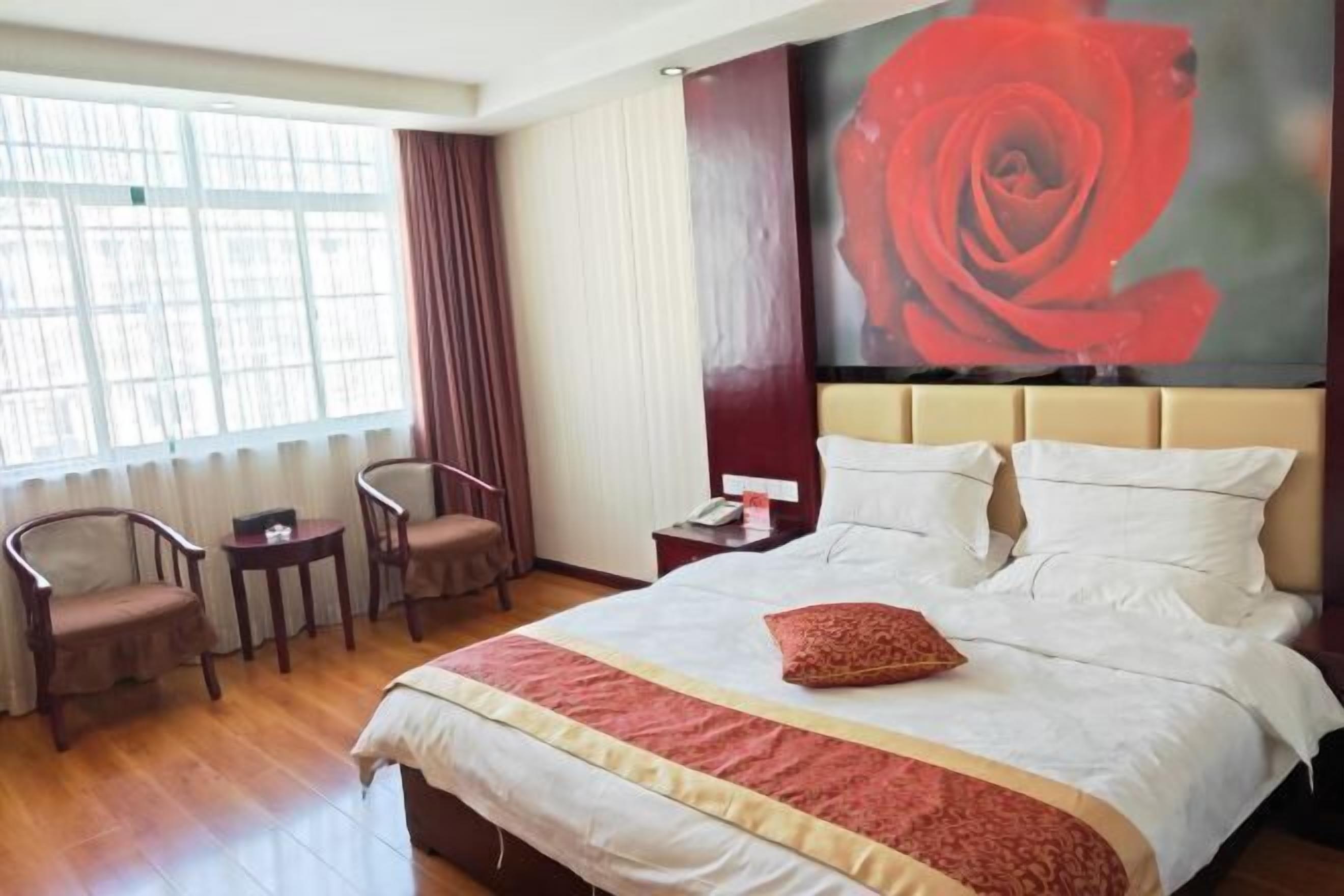 A hotel room with a large bed, a nightstand, a chair, a small table, and a window with curtains.