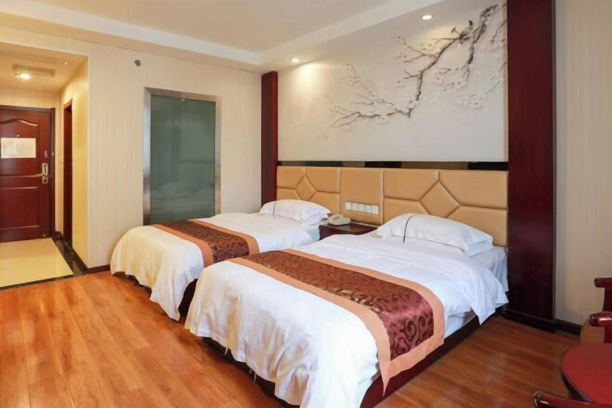 Ein Hotelzimmer mit zwei Betten, Holzboden, Wandbild und einem roten Sessel.