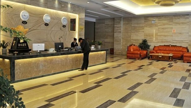 Een hotel receptie met een marmeren vloer, een receptiebalie met computers, een bank en een plant.