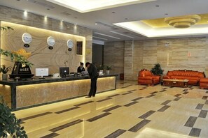 A hotel reception area with a marble floor, a reception desk with computers, a sofa, and a plant. - Huangchao Hotel (Jianhe)