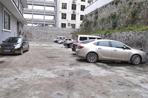 Un espace de stationnement où plusieurs voitures sont garées devant un bâtiment doté d’un mur en pierre et d’une grande structure vitrée en arrière-plan.