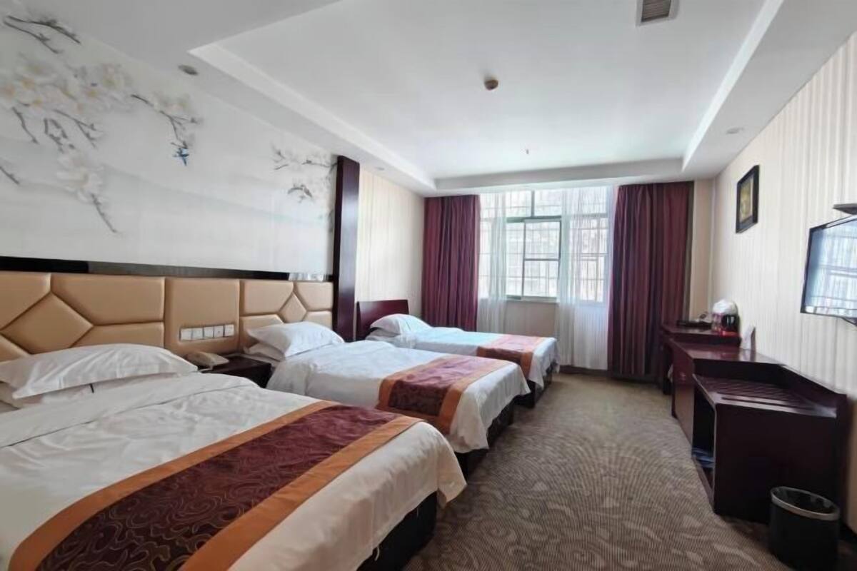 Ein Hotelzimmer mit zwei Betten, einem Schreibtisch, einem Stuhl, einem Fernseher und einem Fenster mit Vorhängen.