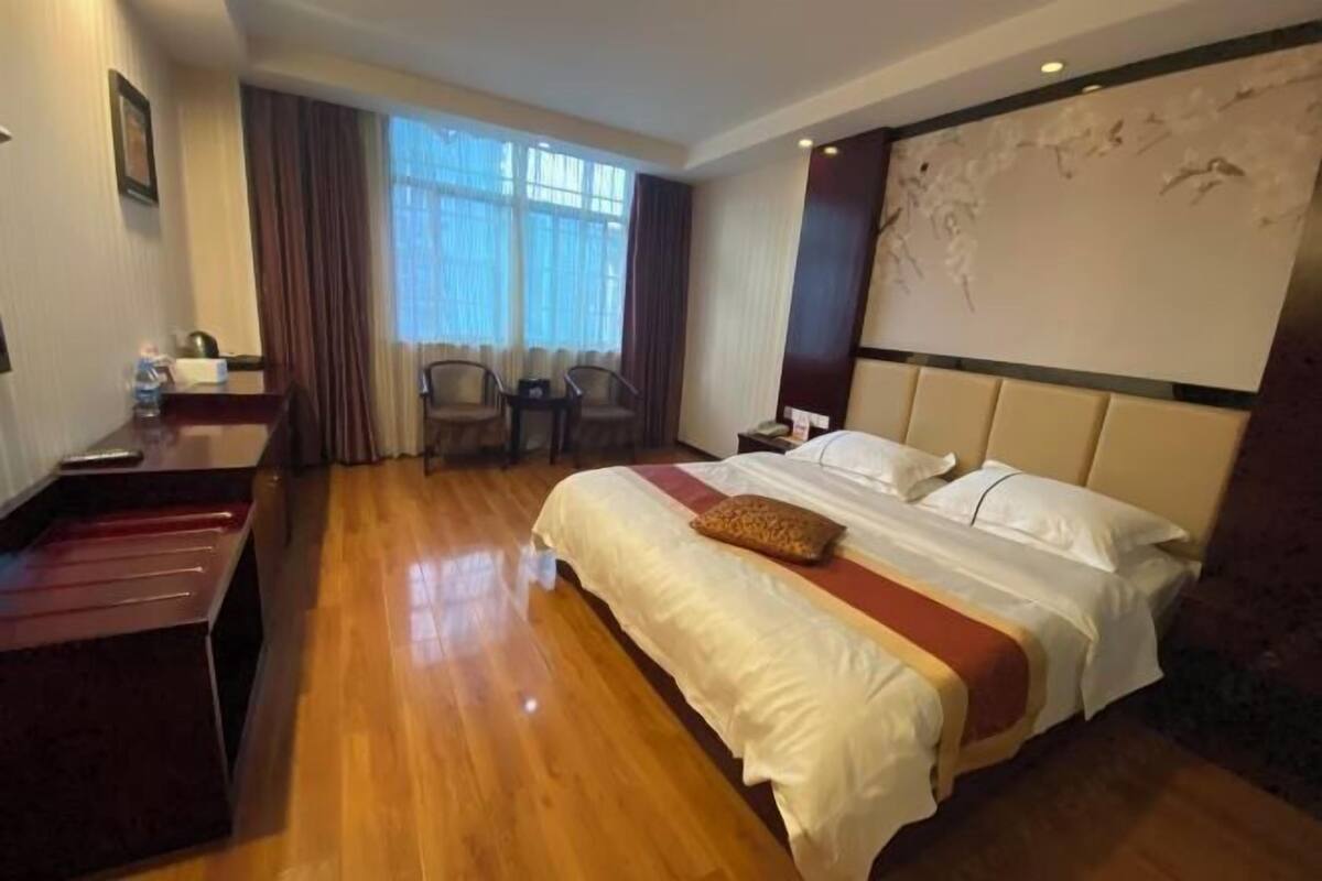 Ein Hotelzimmer mit einem großen Bett, einem Schreibtisch, einem Stuhl, einem kleinen Tisch und einem Vorhangfenster.