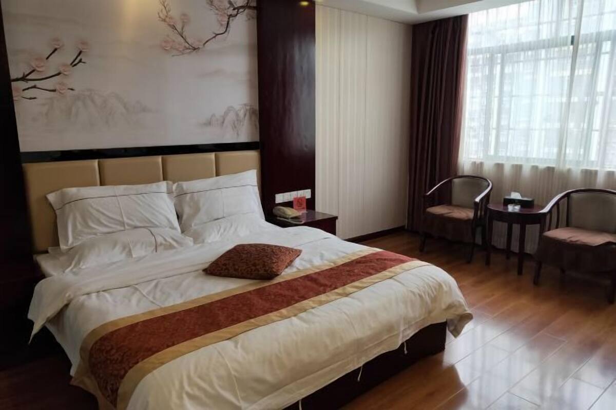 Ein Hotelzimmer mit einem großen Bett, einem Nachttisch, einem Sessel, einem Tisch und einem Fenster mit Vorhängen.