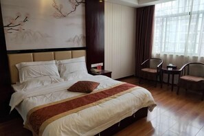Ein Hotelzimmer mit einem großen Bett, einem Nachttisch, einem Sessel, einem Tisch und einem Fenster mit Vorhängen.