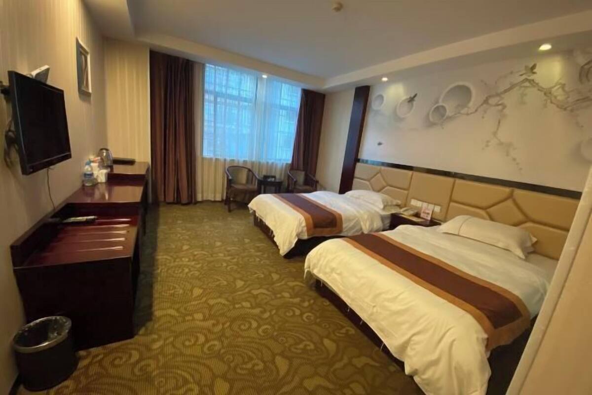Ein Hotelzimmer mit zwei Betten, einem Schreibtisch, einem Stuhl, einem Fernseher und einem Vorhangfenster.
