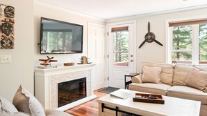 A living room with a fireplace, a television mounted above it, a ceiling fan, and a sofa. - Beautiful property with Mountain View & privacy. Near slopes, trails & eateries! (West Ossipee)