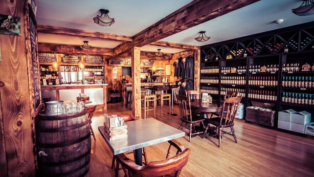 A rustic bar area with wooden beams, a bar counter, and shelves stocked with bottles. - Beautiful property with Mountain View & privacy. Near slopes, trails & eateries! (West Ossipee)