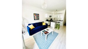 A modern living room with a blue sofa, a white coffee table, and a kitchen in the background. - Apartment with garden, reduced mobility access (Bordeaux)